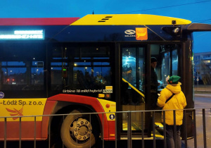 Wolontariusz stoi przed autobusem i wręcza świąteczną kartkę z życzeniami