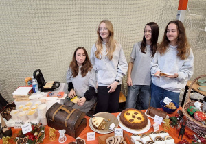 Uczennice stoją przy przygotowanym stoisku ze smakołykami i ozdobami świątecznymi