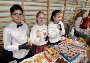 Uczniowie stoją przy przygotowanym stoisku ze smakołykami i ozdobami świątecznymi