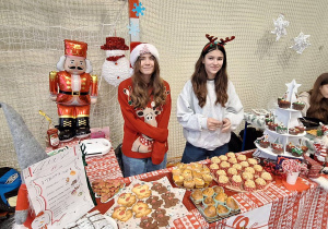 Uczennice stoją przy przygotowanym stoisku ze smakołykami i ozdobami świątecznymi
